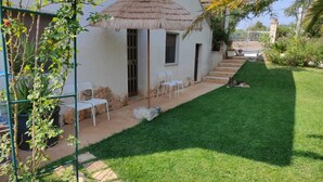 Une maison avec un toit de chaume, un petit patio avec des chaises et une pelouse bien entretenue.