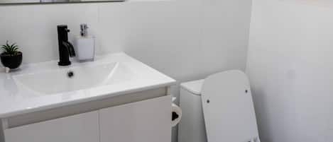 Un baño moderno con un lavamanos blanco, grifo negro y un inodoro.