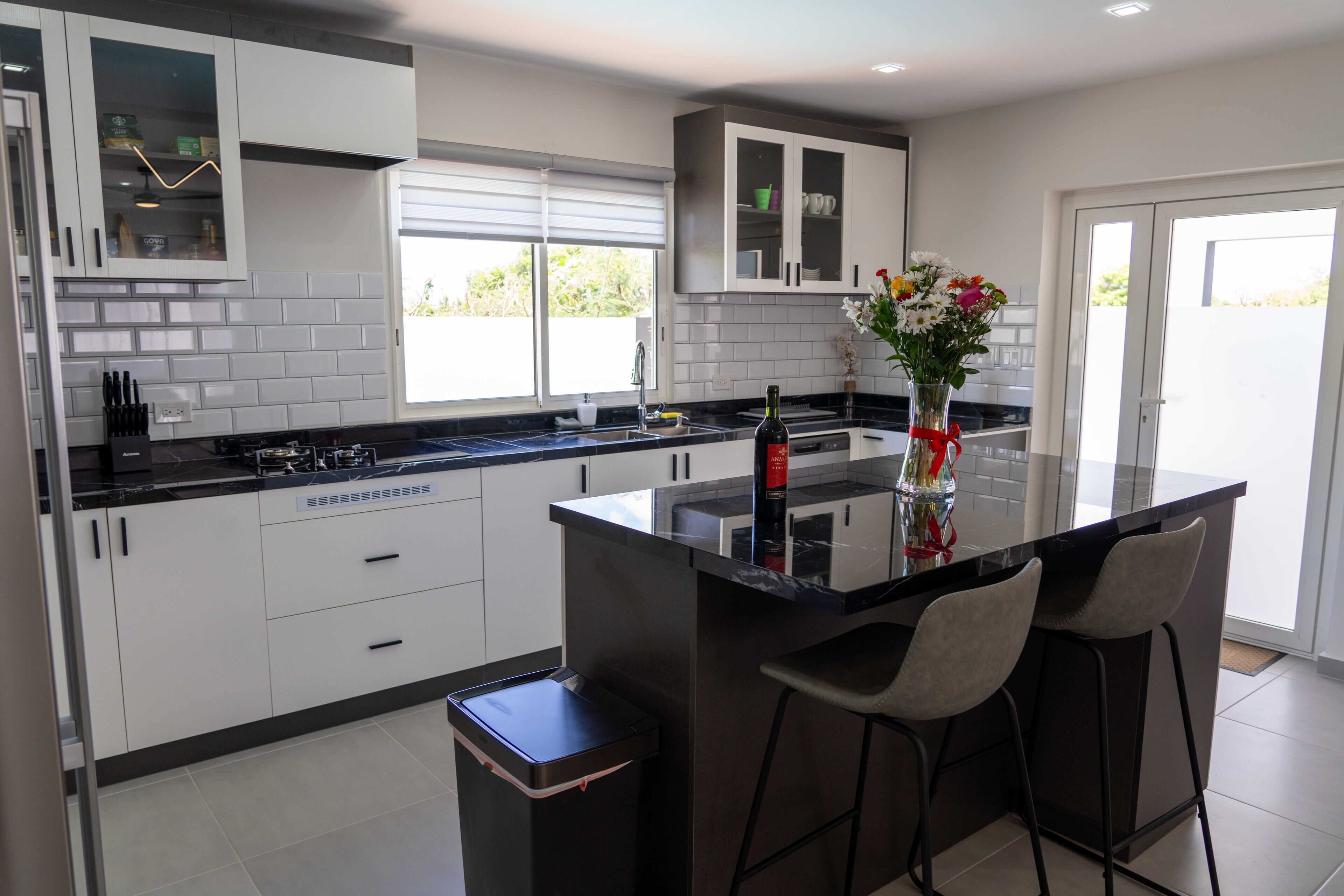 Una cocina moderna con armarios blancos, encimera negra y una isla central con taburetes de bar.