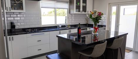 Una cocina moderna con armarios blancos, encimera negra y una isla central con taburetes de bar.