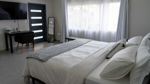 Un dormitorio moderno con cama, escritorio, silla y un amplio ventanal con cortinas translúcidas.