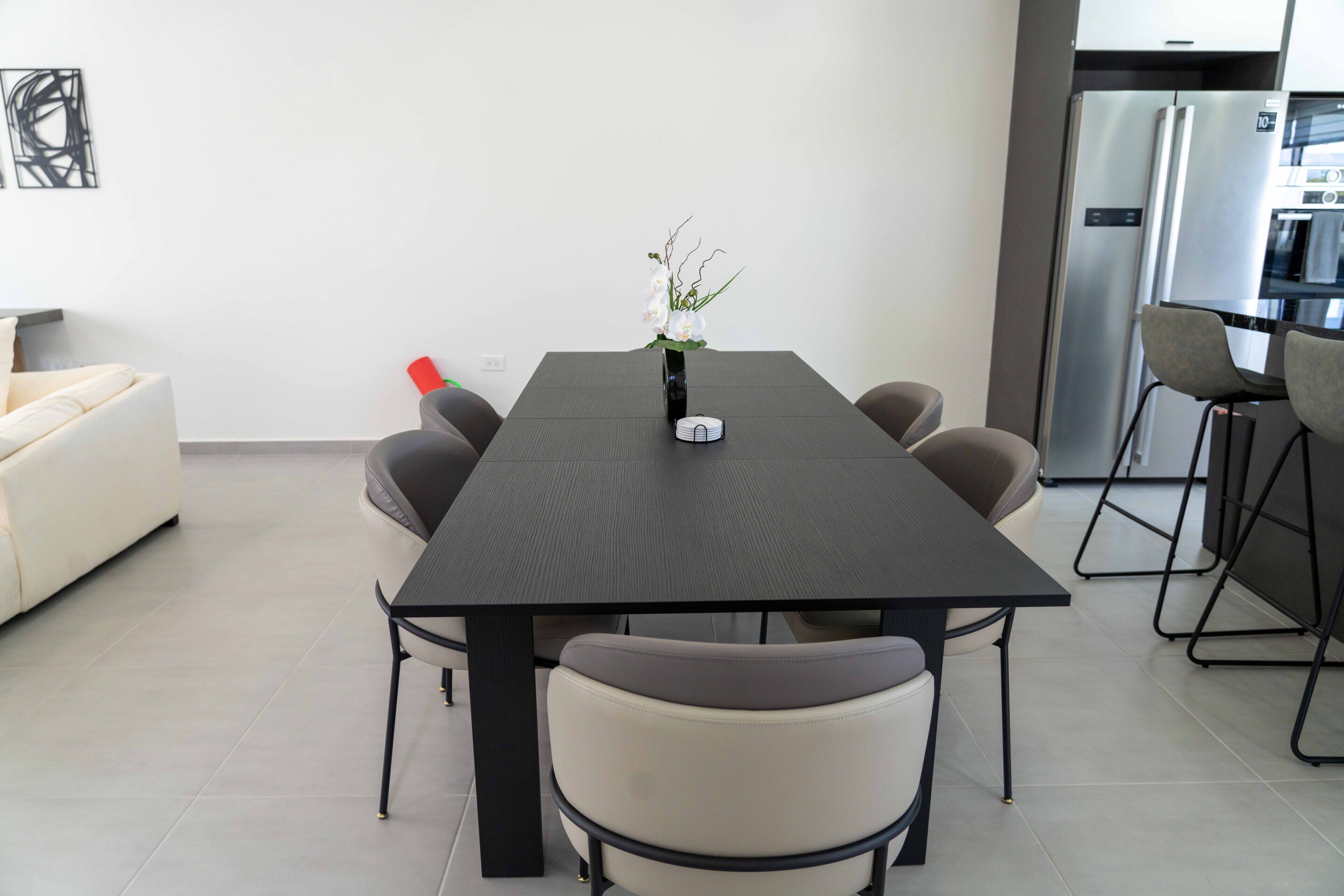A modern kitchen with a dark wooden table, six chairs, and a refrigerator.