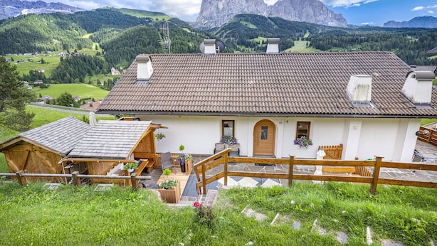 Een traditionele chalet met een pannendak, houten balkon en uitzicht op een bergketen.