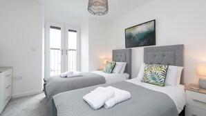 Quarto de hotel moderno com duas camas, uma janela grande e um lustre.