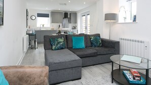 Uma sala de estar moderna com um sofá modular cinza, uma mesa de centro de vidro e vista para a área da cozinha.