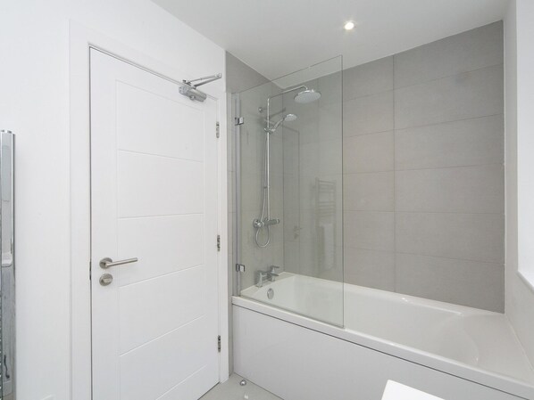 A modern bathroom with a glass-enclosed shower, a white bathtub, and a door with a handle. - Modern 2 bed Apartment in Rhosneigr - Pass the Keys (Rhosneigr)