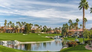 A golf course with a pond, palm trees, and a building with a red roof.