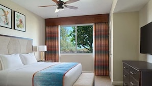 A hotel room with a bed, a bench, a dresser, a ceiling fan, and a window with curtains.