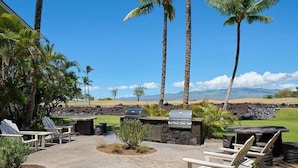 An outdoor patio with a grill, seating, and palm trees.