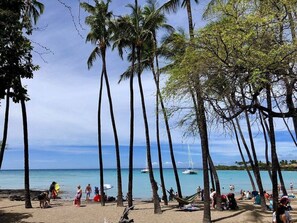 Ein Strand mit hohen Palmen, entspannten Personen und Booten im Wasser.