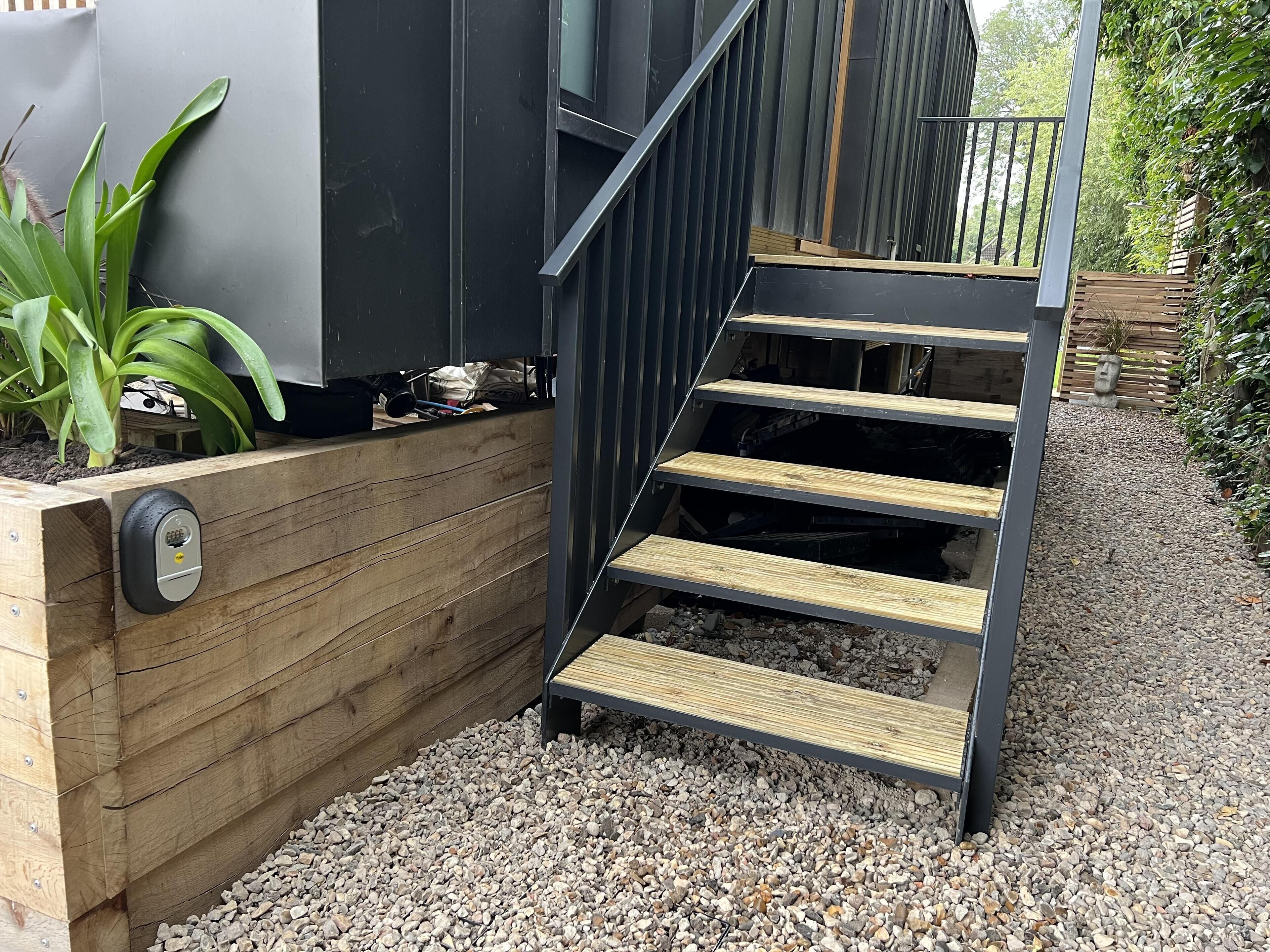 Una moderna scala esterna con gradini in legno e ringhiere in metallo, che conduce a un'area terrazzata in legno.