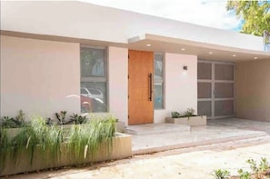 A modern building with a large glass door, a wooden door, and a small planter with plants.