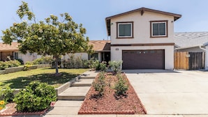 A two-story house with a garage, a well-maintained lawn, and a tree in the front yard. - Studio Suite with Private, Secured Entrance, No Shared Spaces, Driveway Parking  (Spring Valley)