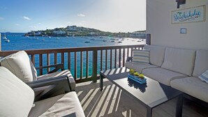 A balcony with a view of the sea, a sofa, a table with a plant, and a sign reading "Beachaholic". - Oceanfront Cowpet Bay Condo Beach, Pool & Generator (St Thomas)