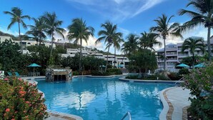 A swimming pool with a stone border, surrounded by palm trees and a clear blue sky. - Oceanfront Cowpet Bay Condo Beach, Pool & Generator (St Thomas)