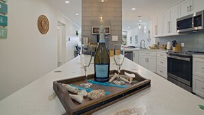 A modern kitchen with white cabinetry, a central island with a wine bottle and glasses, and a hanging light fixture. - Oceanfront Cowpet Bay Condo Beach, Pool & Generator (St Thomas)