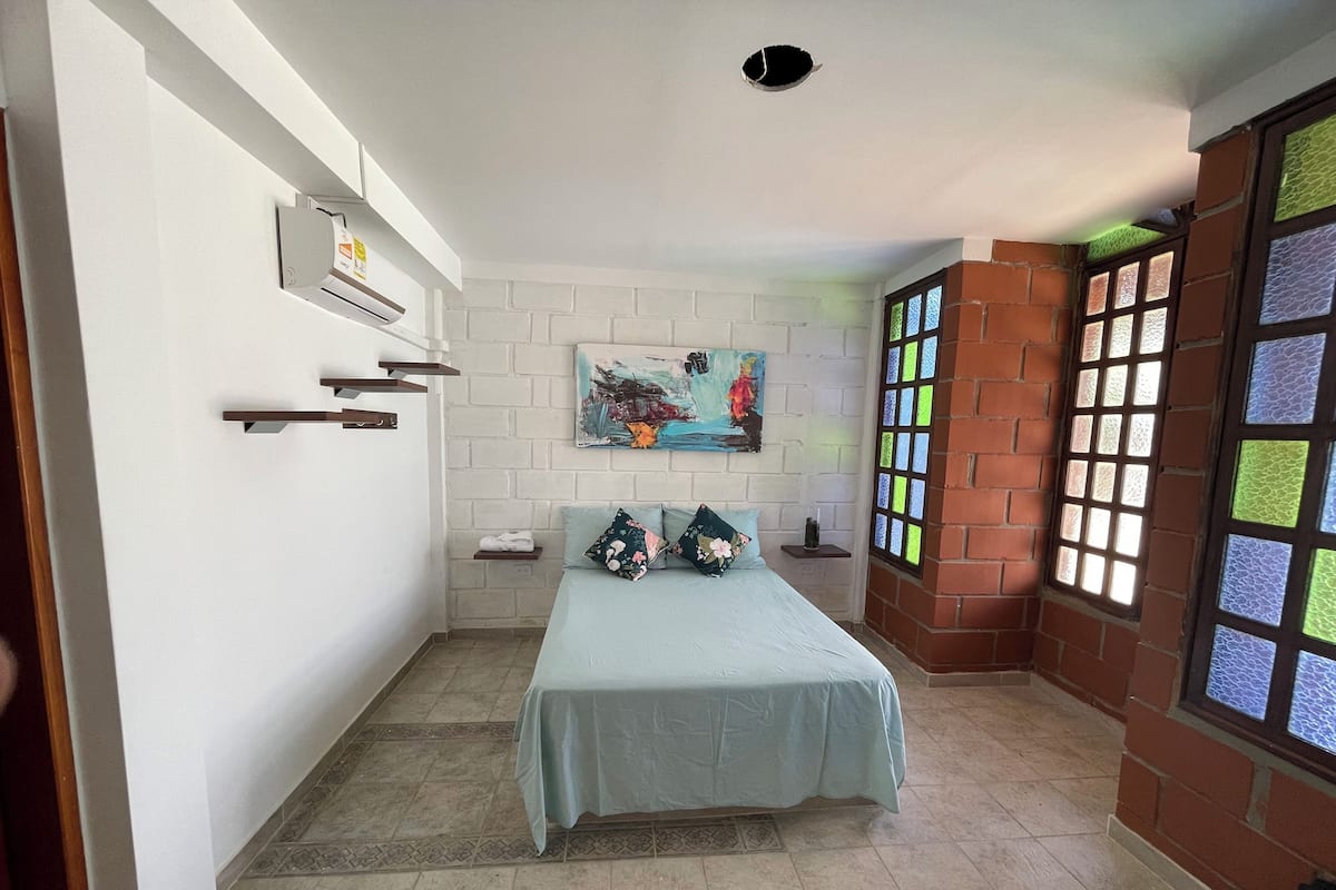 Une chambre à coucher avec un lit, un tableau au mur, une fenêtre avec des vitraux et un mur en briques.