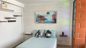 A bedroom with a bed, a nightstand, a wall-mounted air conditioner, a painting, and a brick wall.