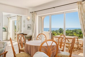 Un espace repas comprenant une table et des chaises, une vue sur la mer et un balcon avec une table et des chaises en bois.