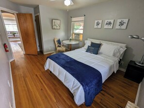 A bedroom with a bed, a chair, a small table, and a window.