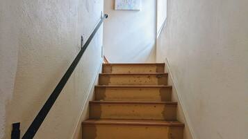 Un escalier avec des marches en bois et une rampe noire, menant à un palier où est accrochée une image encadrée au mur.