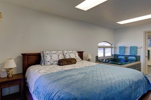 A bedroom with a bed, a nightstand, a lamp, a window, and a bathtub. - Queen Bee - Beach Front w/ Vast Ocean Views, Spa (Gold Beach)
