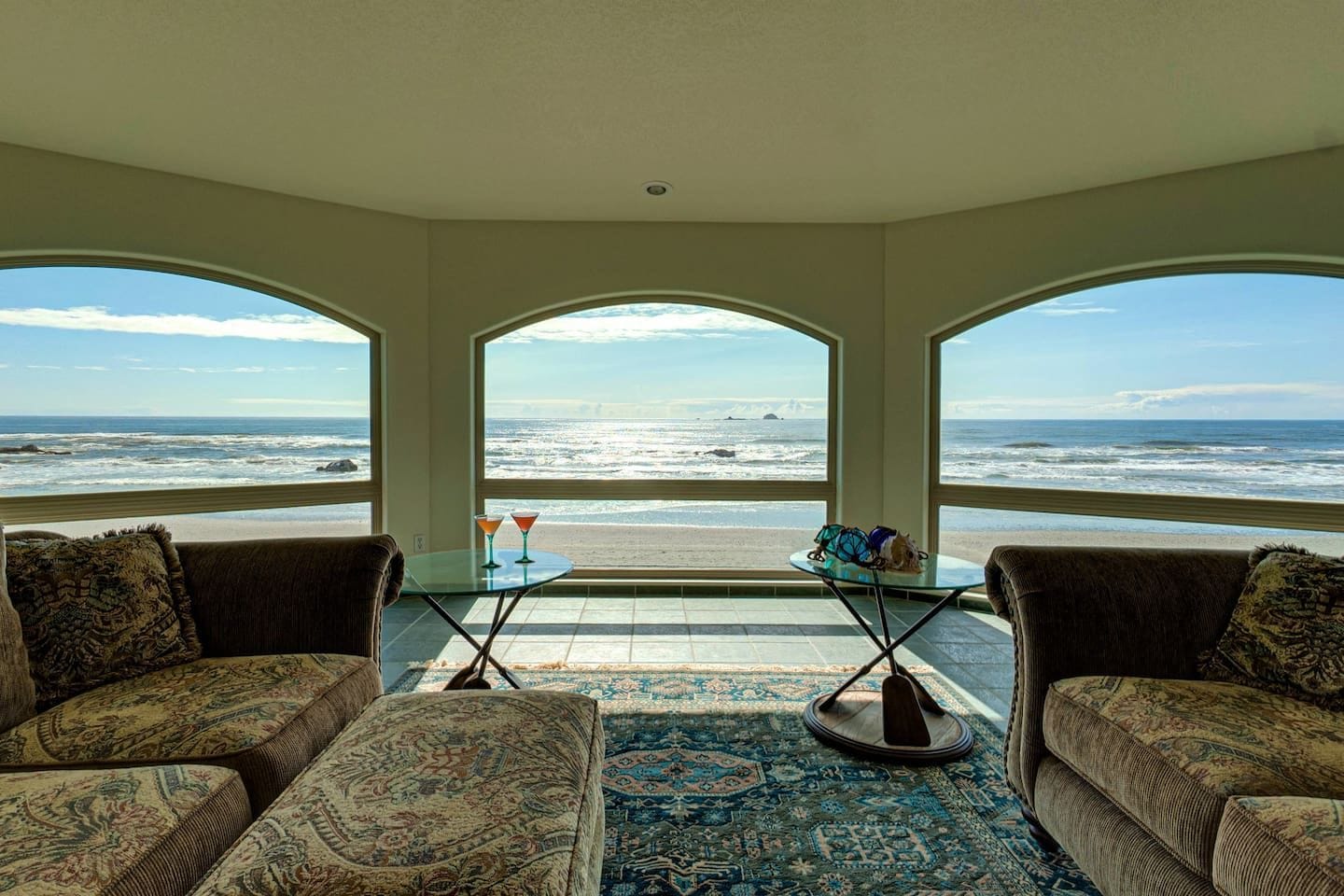 A room with a view of the ocean, furnished with two sofas and a small table with drinks.