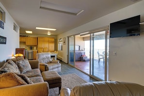 A living room with a sofa, ottoman, and a television mounted on the wall. - Queen Bee - Beach Front w/ Vast Ocean Views, Spa (Gold Beach)