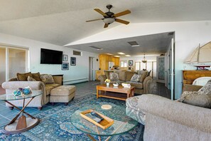 A spacious living area with a ceiling fan, a large sofa set, a coffee table, and a patterned rug.
