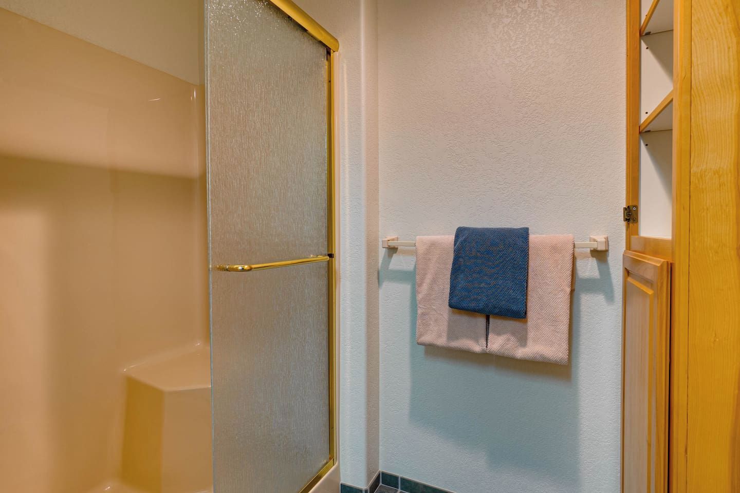 A bathroom with a shower door, a towel rack with a towel, and a wooden door frame.
