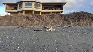 Uma casa à beira-mar com varanda curva, vista para a praia e um morro ao fundo.