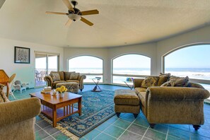 A spacious living room with a large window overlooking the ocean, furnished with a sofa, armchairs, and a coffee table. - Queen Bee - Beach Front w/ Vast Ocean Views, Spa (Gold Beach)