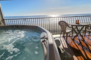 A hot tub with a view of the ocean, a table with chairs, and a railing.