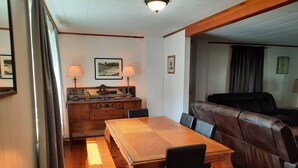 Un coin repas avec une table et des bancs en bois, un canapé en cuir et un meuble contenant des objets décoratifs.