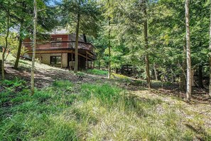 A cabin with a wooden deck and a large window, surrounded by dense forest. - Peaceful, Woodland Retreat in Frankfort, MI Near Crystal Lake & Sleeping Bear (Frankfort)