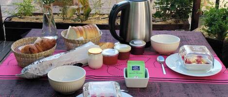 A breakfast setup with bread, pastries, jams, and a coffee pot on a table.