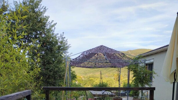 A wooden deck with a table and chairs, surrounded by plants and a pergola. - La Guitoune de Laroque (LAROQUE)