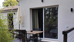A patio with a table and chairs, a wooden deck, and a sliding glass door. - La Guitoune de Laroque (LAROQUE)