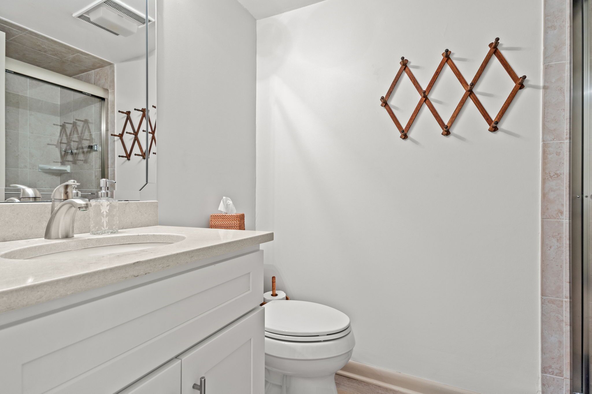 Ein modernes Badezimmer mit einem weißen Waschbecken, einem Spiegel und einer Toilette. Über der Toilette befinden sich dekorative Holzwandbehänge.