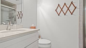 Ein modernes Badezimmer mit einem weißen Waschbecken, einem Spiegel und einer Toilette. Über der Toilette befinden sich dekorative Holzwandbehänge.