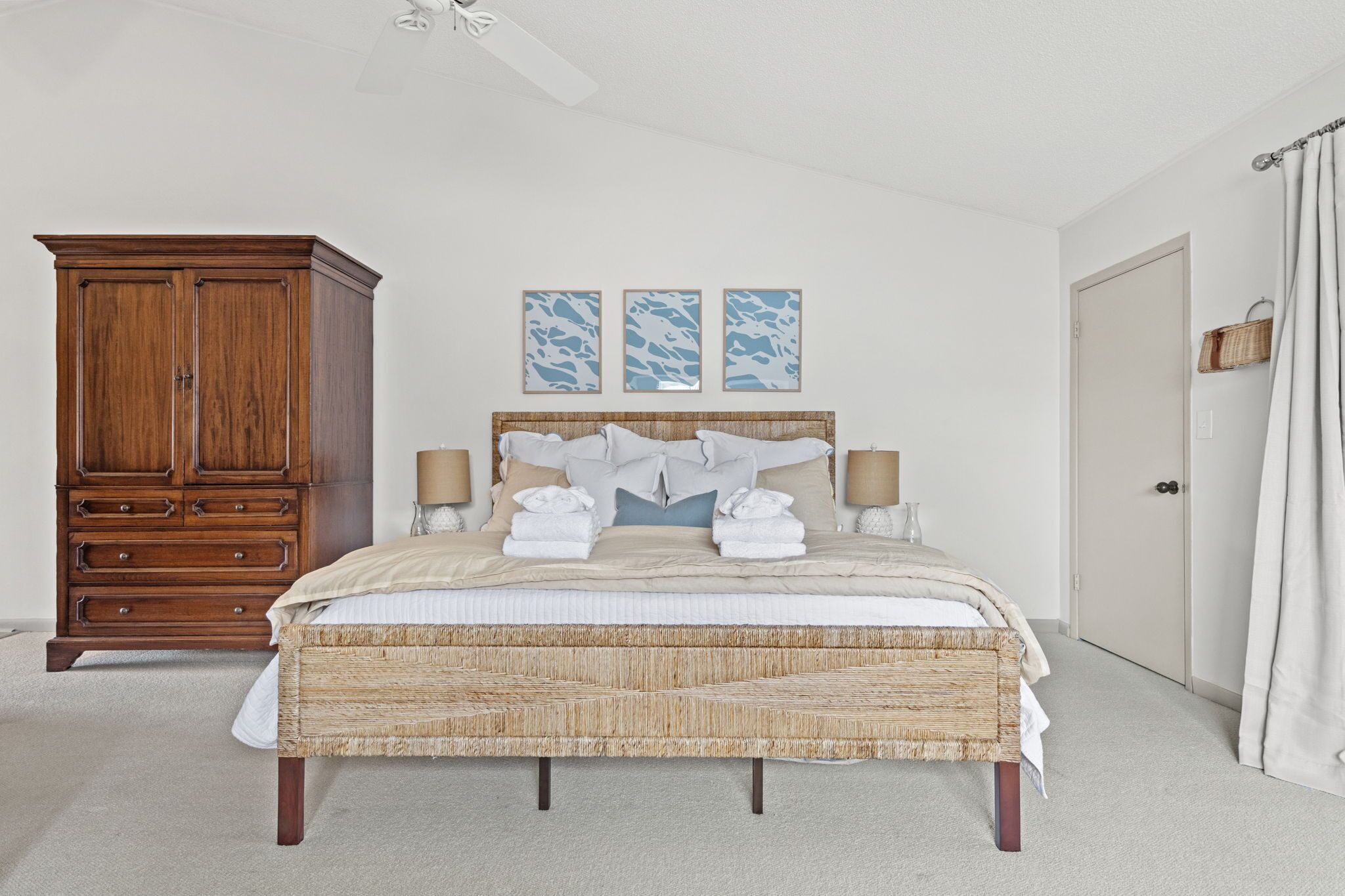 A bedroom with a large wooden dresser, a bed with a woven headboard, and three wall-mounted artwork pieces.