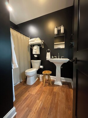 A modern bathroom with a black wall, white fixtures, and a wooden floor.