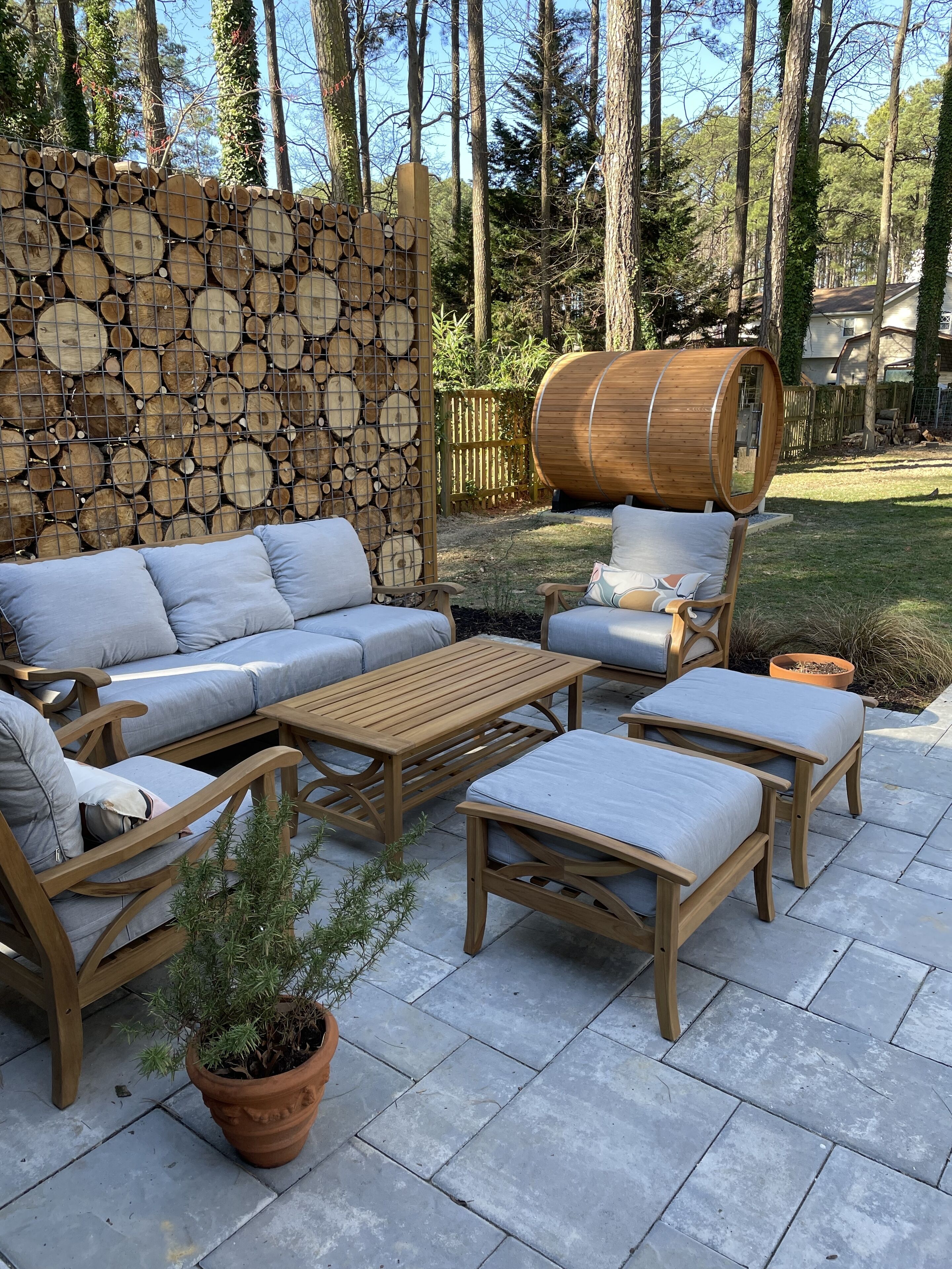 Un espace extérieur aménagé en terrasse, avec un ensemble de canapés en bois, une table en bois et un tonneau.