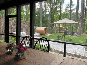 A covered patio with a wooden table and chairs, a stone wall, and a view of a backyard with a wooden barrel, outdoor furniture, and a hammock.