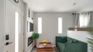 Ein modernes Wohnzimmer mit einem grünen Sofa, einem Couchtisch aus Holz mit einer Vase voller gelber Blumen und einem flachbildfernseher an der Wand.