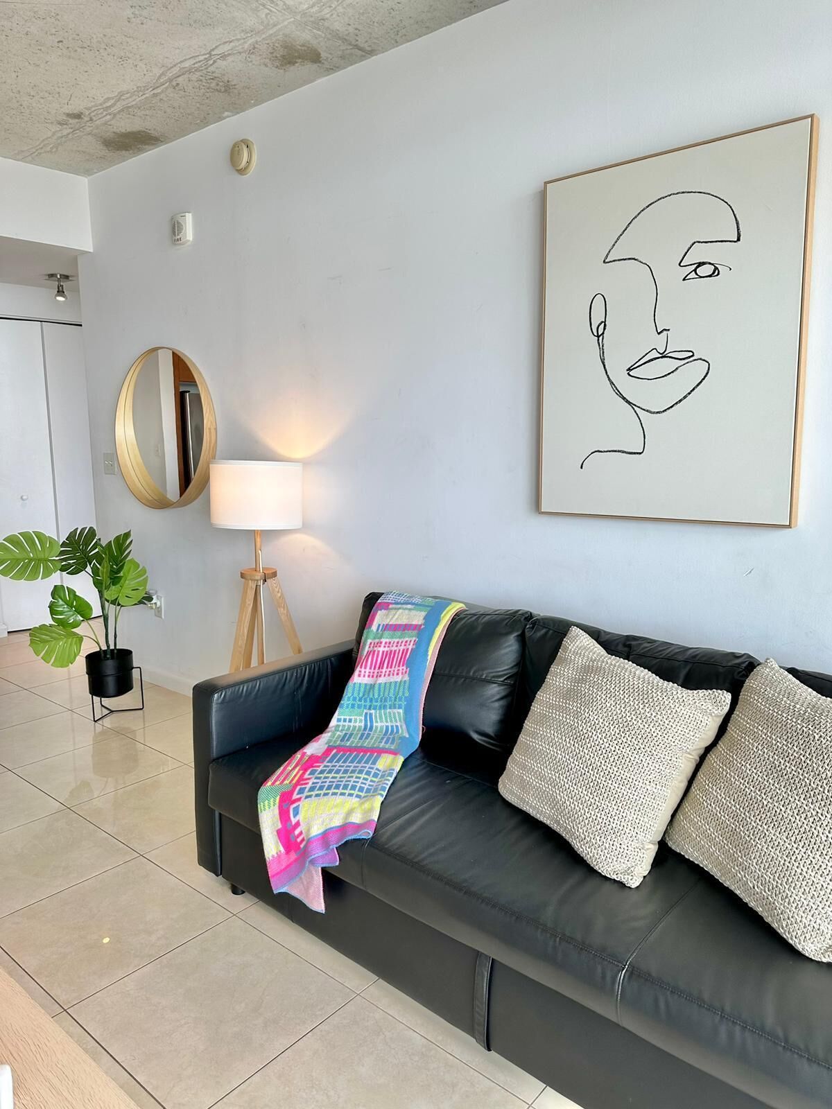 Ein modernes Wohnzimmer mit einem schwarzen Ledersofa, einer bunten Decke und einem minimalistischen abstrakten Gemälde.