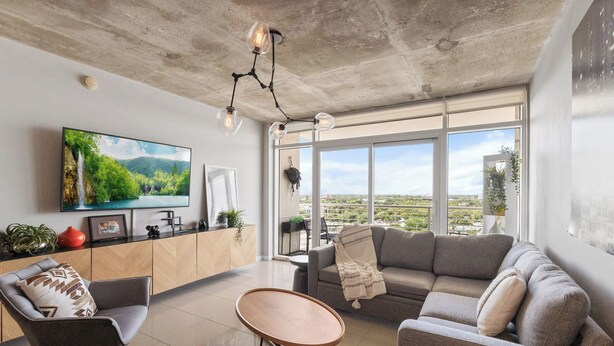 Un salon moderne doté d’un grand téléviseur, d’un canapé, d’une table basse et offrant une vue sur le paysage urbain grâce à de grandes fenêtres.