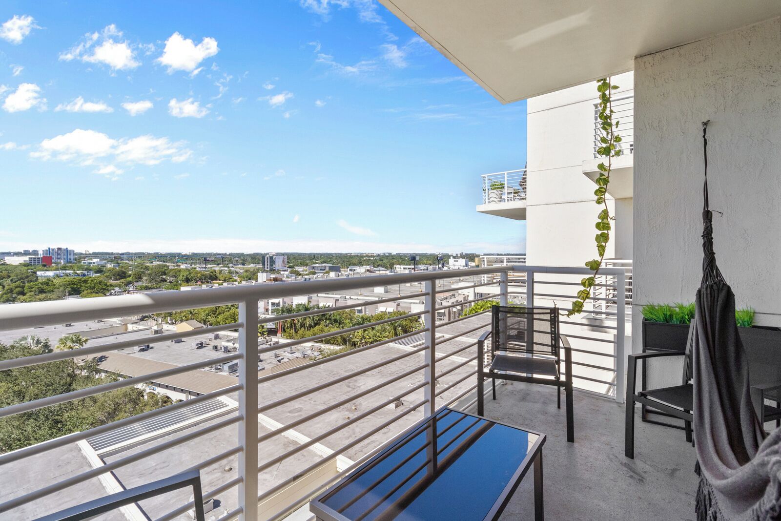 A balcony with a view of the city, a table, chairs, and a hanging plant.