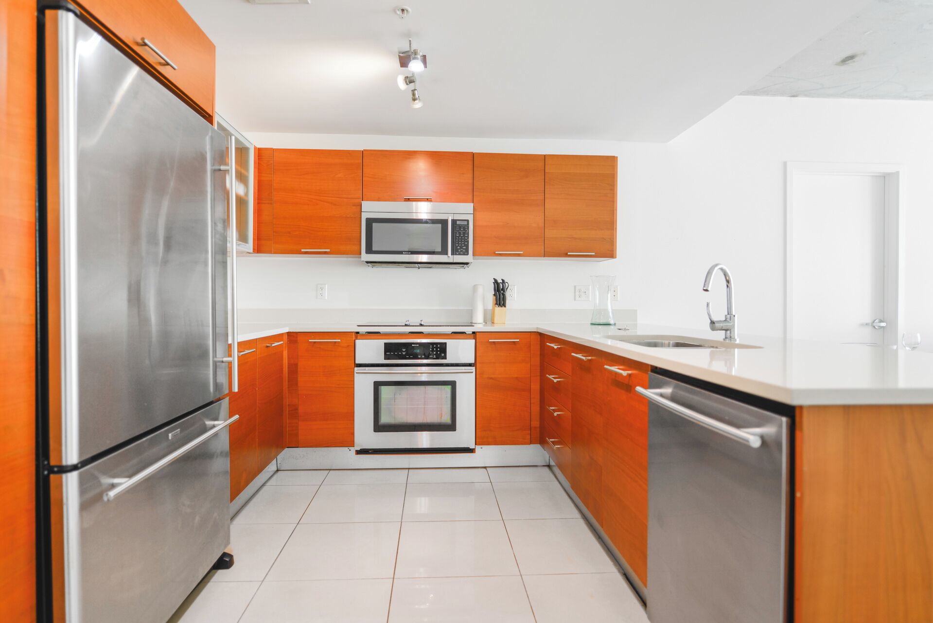 A modern kitchen with stainless steel appliances, wooden cabinets, and a white countertop.
