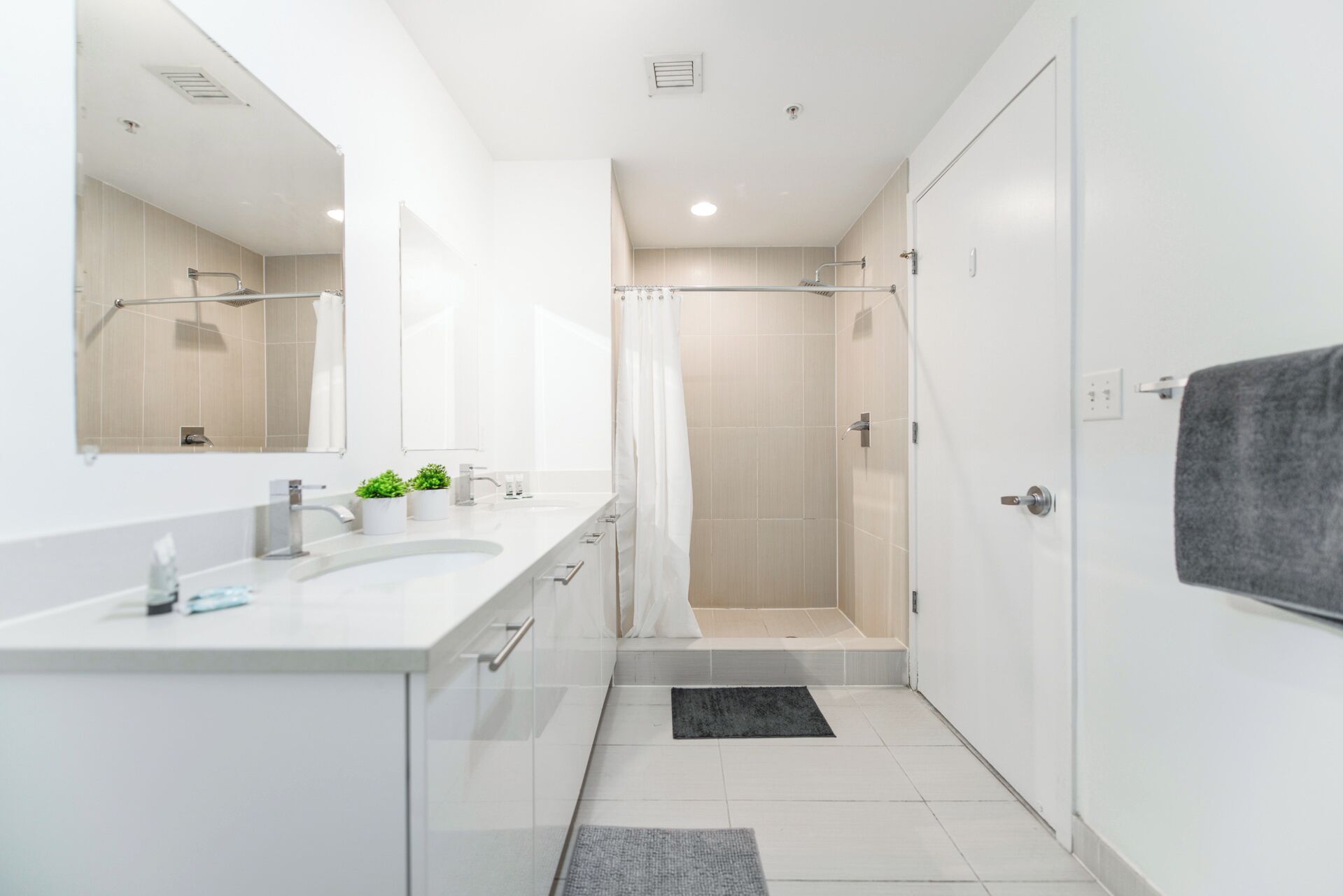 A modern bathroom with a white vanity, a shower, and a towel hanging on the wall.